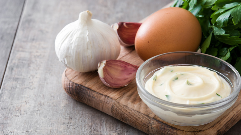 Aioli in a clear small bowl, surrounded by its ingredients