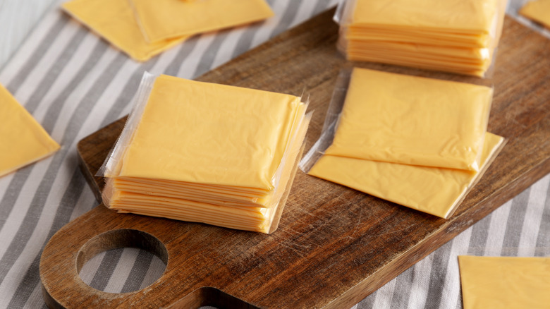 Wrapped individual slices of American cheese on a wooden cutting board