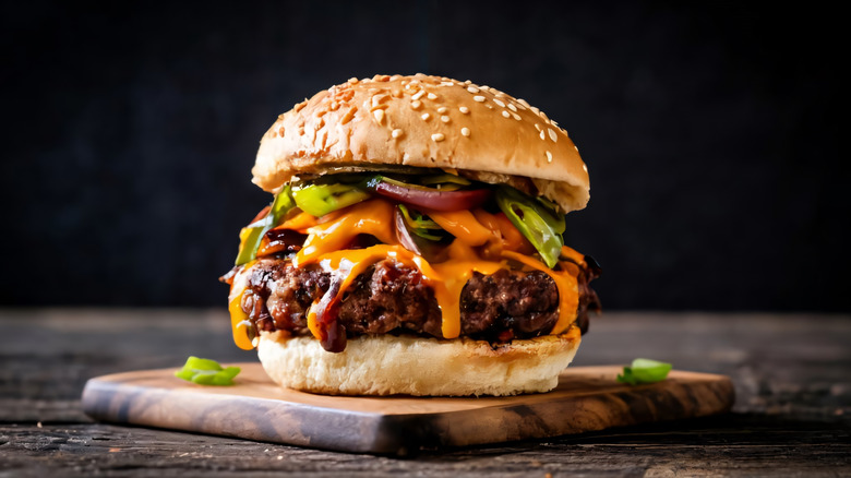 Thick juicy burger in seeded bun with multiple condiments on top