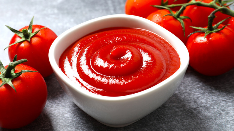 Ketchup in a white bowl with fresh tomatoes in the background