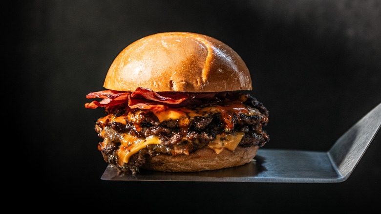 Close up of burger with multiple condiments on top, on a spatula
