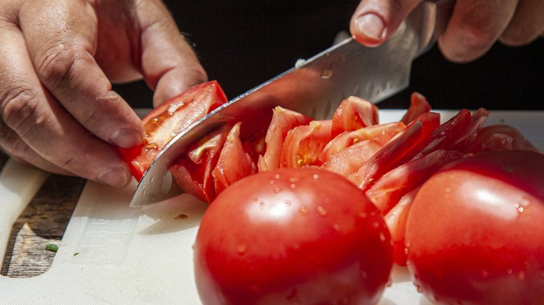 Person slicing fresh tomatoes with sharp knife