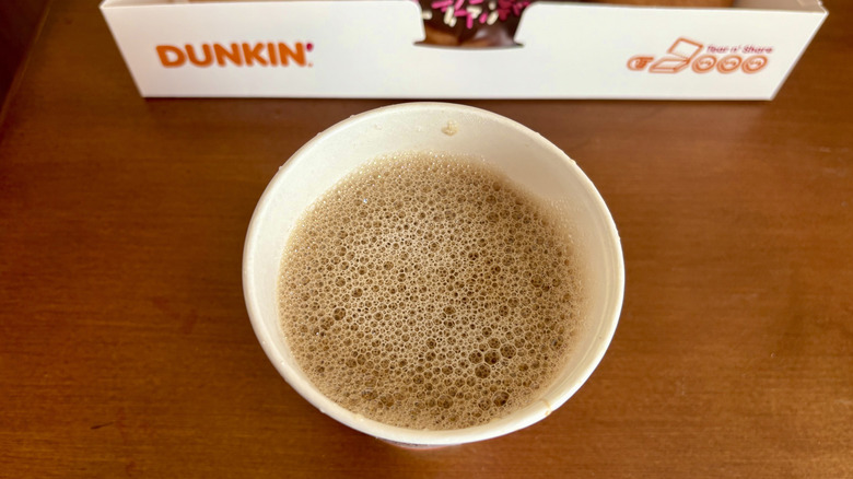 A macchiato from Dunkin' in front of a donut box on a wood surface