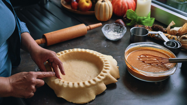 A woman places a pie crust in a pie pan, bowl of pie filling nearby