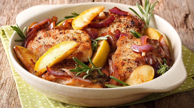 Cooked pork chops, red onions, and sliced apples in a white casserole dish