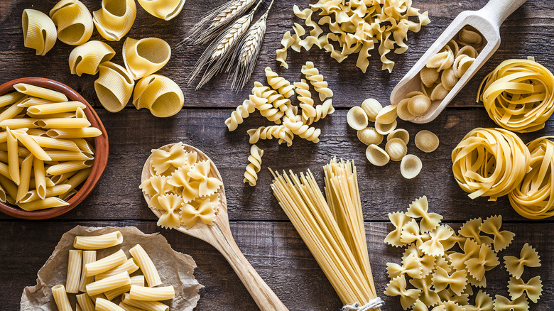 A variety of types of dried pasta displayed on a wooden table
