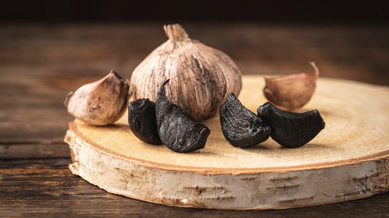 four cloves of black garlic sitting on a wooden chopping board with a full clove in the background