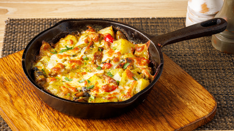 A cast iron skillet with fried potatoes mixed with vegetables and covered in melted cheese.