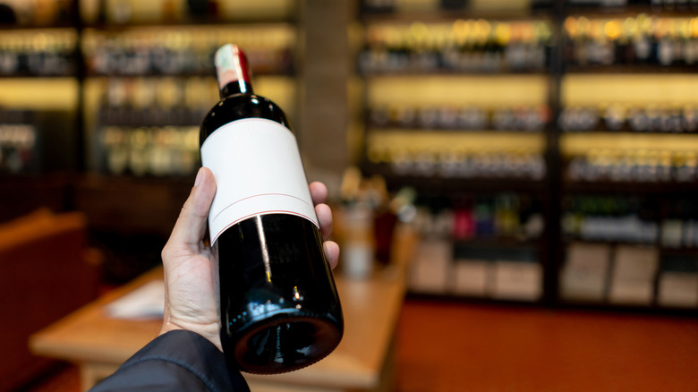 A sommelier holding a bottle of red wine in a wine cellar.