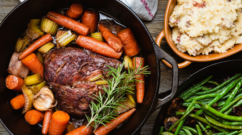 A pot roast cooked with carrots, celery, garlic, and herbs in a cast iron pan