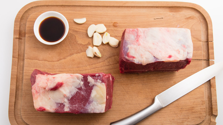 Raw chuck roast sits on cutting board with soy sauce and garlic cloves