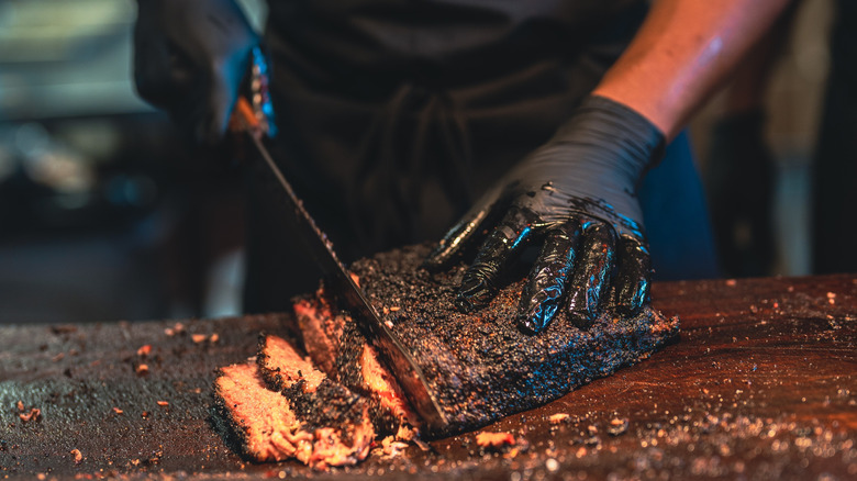 Two gloved hands slicing thick pieces of juicy, charred brisket
