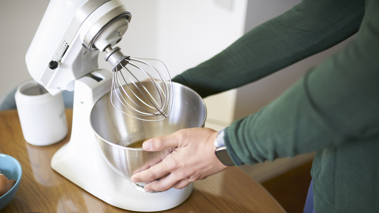 A person adjusting the bowl of a white KitchenAid mixer
