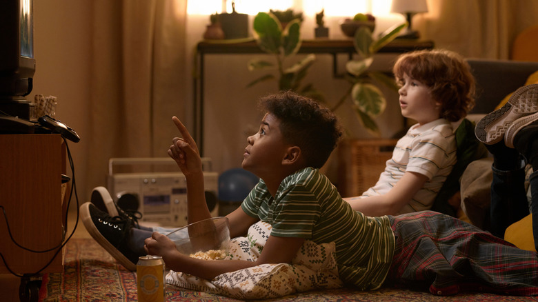 Two boys watching TV with a bowl of snacks in a 90s-style living room