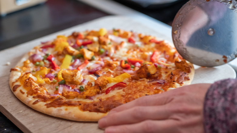 Person about to slice a thin crust pizza on a cutting board with a pizza cutter