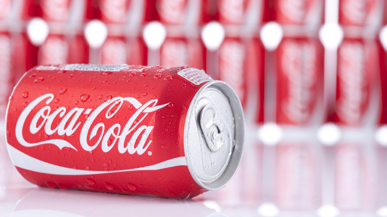 A can of Coke on its side in front of rows of Coke cans