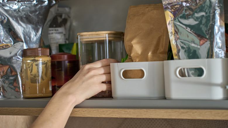 Hand reaching into an organized kitchen cabinet with baskets