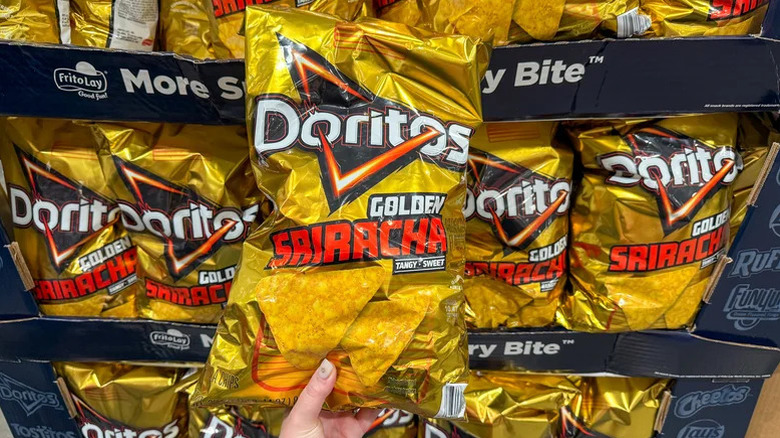 Person holding a bag of Doritos Golden Sriracha in front of a display of the chips