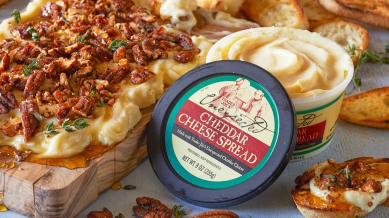 A tub of Trader Joe's Unexpected Cheddar spread sits open next to a charcuterie board