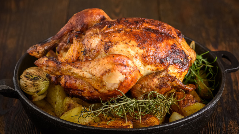 Roast chicken in a cast iron pan with vegetables and rosemary.