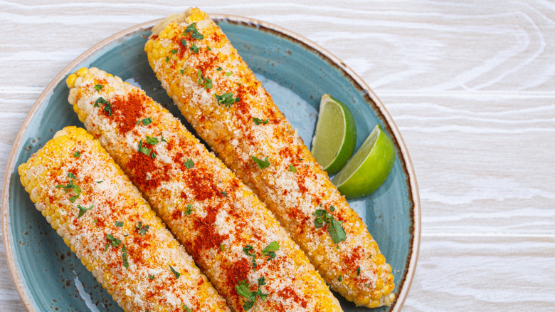 Elote with lime slices on blue plate
