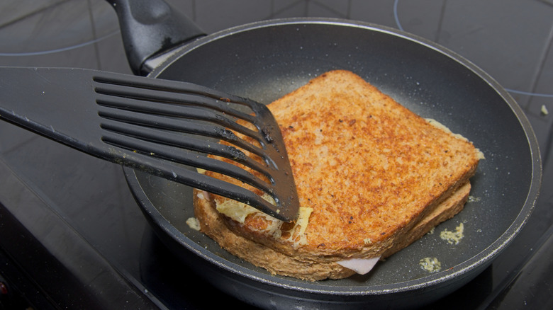 A grilled ham and cheese sandwich being cooked in a pan