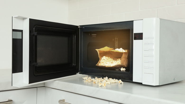 Popcorn spilling out of a bag inside of an open microwave