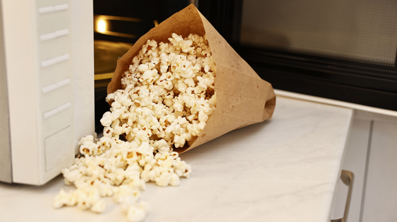 Tasty popcorn in paper bag near microwave oven on white marble countertop indoors,