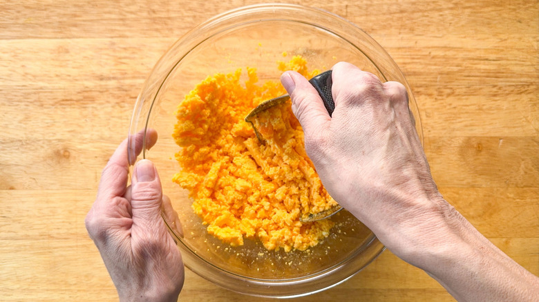Mashing hard boiled egg yolks in glass bowl with pastry cutter