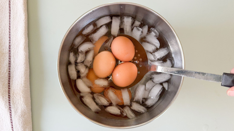Brown eggs in slotted spoon over ice bath in stainless steel bowl