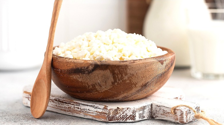 Cottage cheese in a wooden bowl atop a white-washed wooden serving board