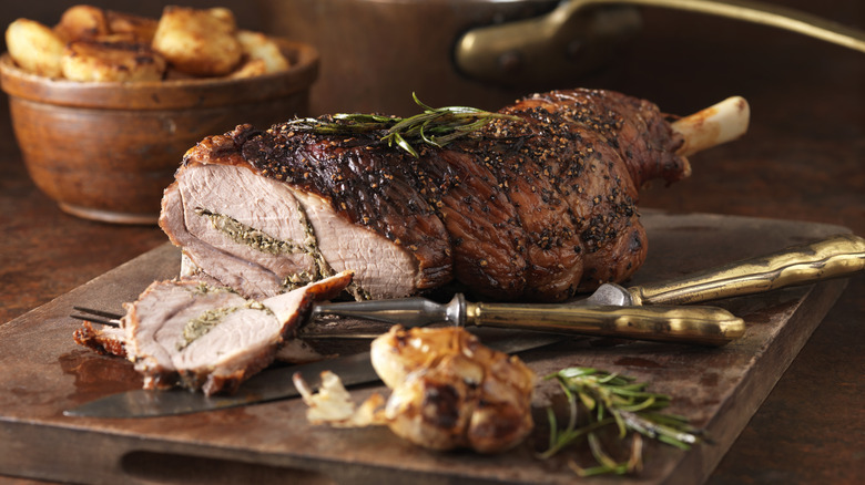 A partially sliced roast leg of lamb on a wooden cutting board.