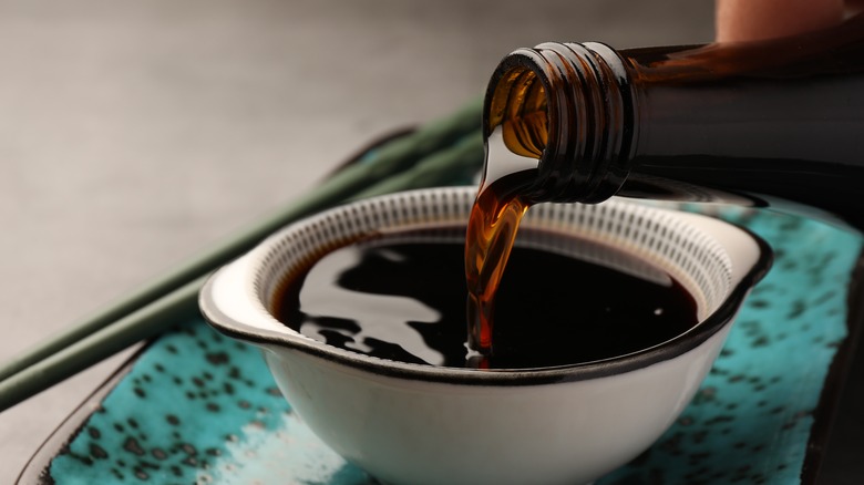 Soy sauce being poured from a bottle into a bowl.