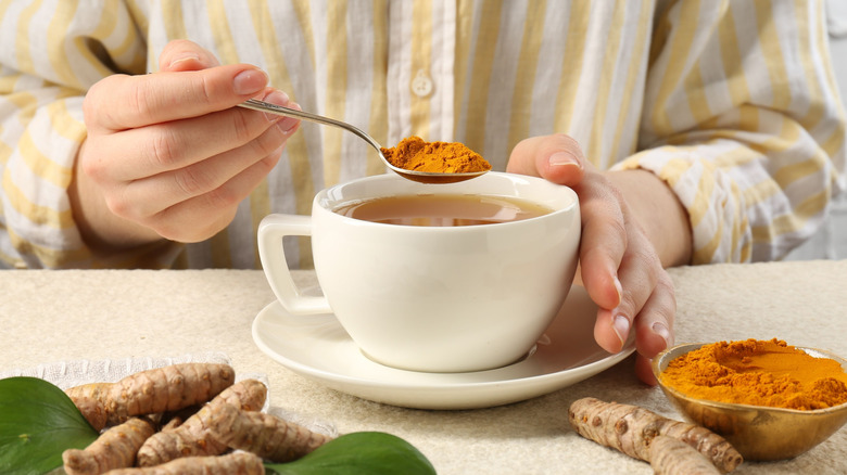 Holding turmeric powder over a cup of tea