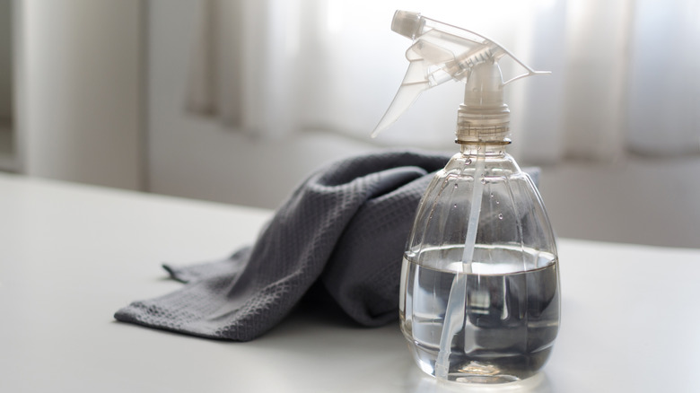 Spray bottle filled with pure water and vinegar and a cleaning cloth on a table against a bright window all in white and gray color. Environmentally friendly eco cleaning products concept