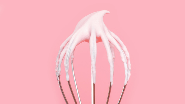 Close up of whisk with cream on it over a pink background.