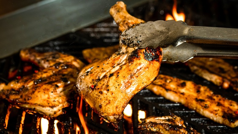 Tongs holding up cooked chicken leg quarters on the grill.