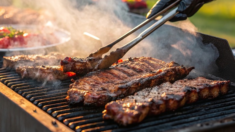 Hand holding tongs picking up barbecued ribs on the grill