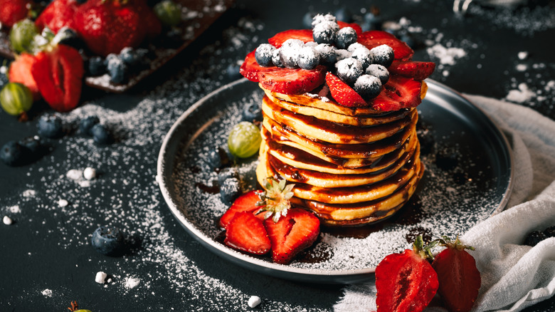 Stack of pancakes with fruit, syrup, and powdered sugar