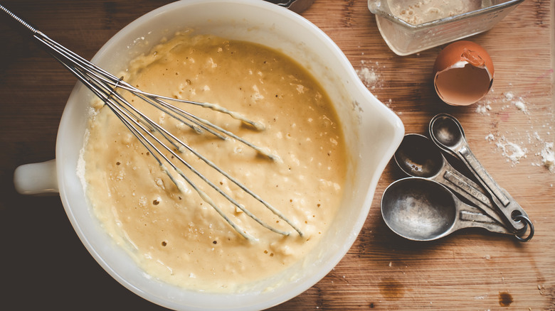 Pancake batter in mixing bowl next to measuring spoons and eggshells