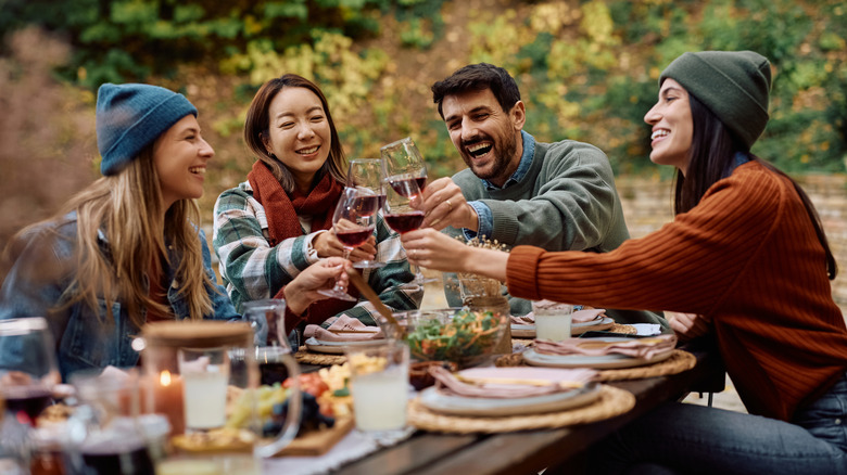 Four people toasting with wine at a long picnic table outdoors.