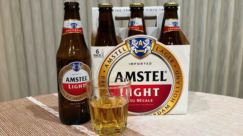 A glass half-full with Amstel Light on a table next to a six-pack of Amstel Light