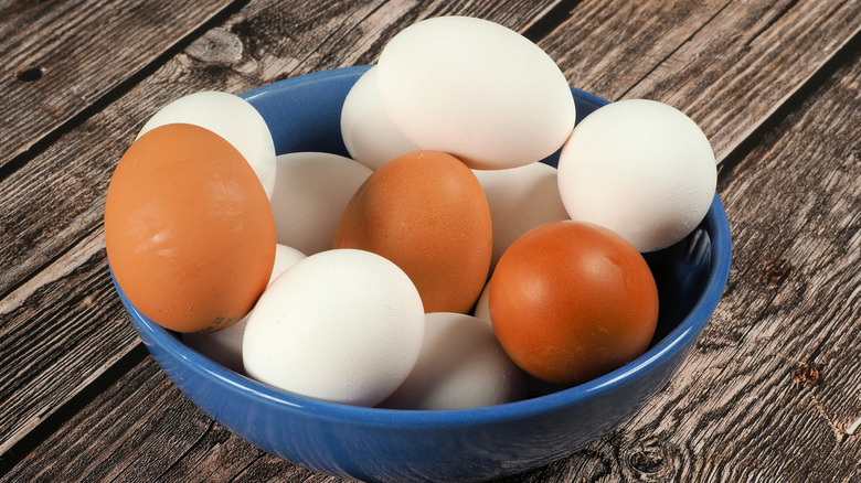 A mix of white and brown eggs in a blue bowl on a wooden table