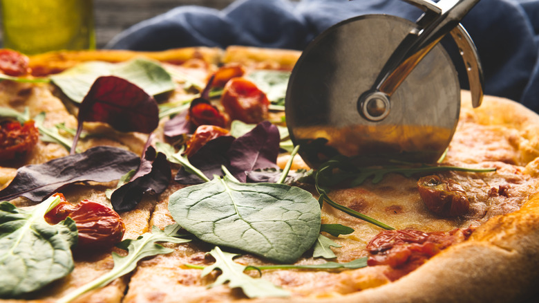 Pizza cutter slicing a pizza.