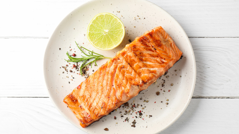 A seasoned salmon on a white plate with fresh garnish and a slice of lemon on the side