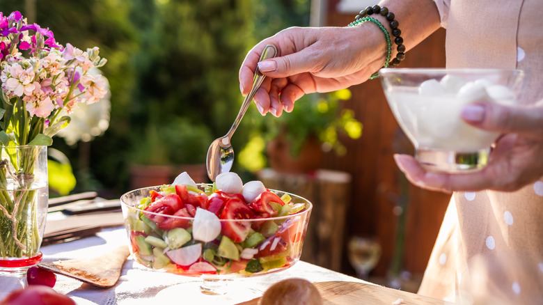 Person adding mozzarella balls to a vegetable salad