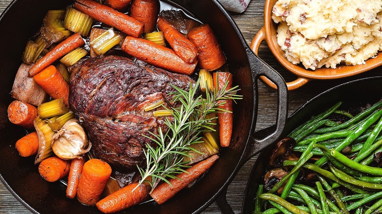 Pot roast with chopped carrots, celery, garlic and fresh rosemary in a cast iron skillet