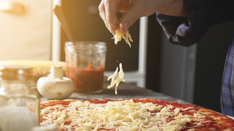 Hand sprinkling cheese on a pizza