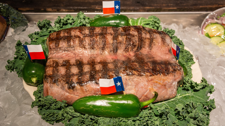 The famous 72-ounce steak customers of The Big Texan steakhouse on a plate with green garnish, peppers, and Texas flags