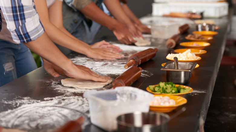 Group of people rolling pizza dough